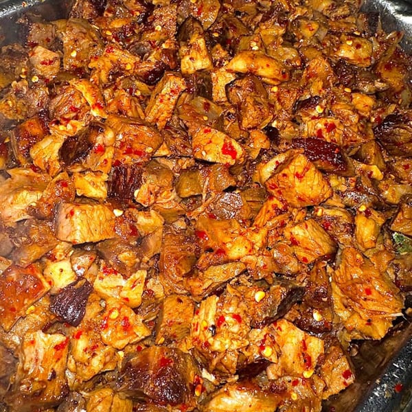 Close-up of seasoned, diced meat with red chili flakes, likely for Mexican cuisine.
