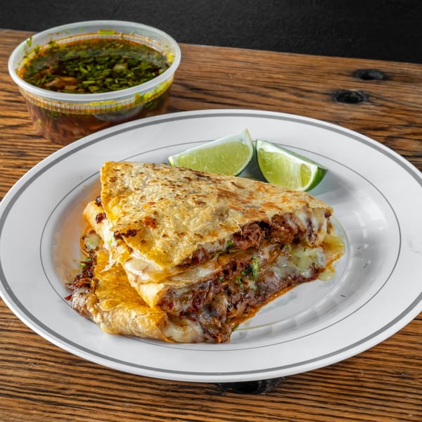 Chilango Taco Loco's birria quesadilla with melted cheese, limes, and a side of consommé.