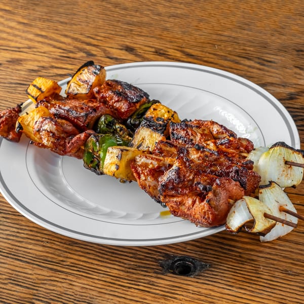 Two grilled chicken and vegetable skewers with pineapple, bell peppers, and onions on a white plate.