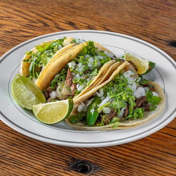 Three Chilango Taco Loco tacos with meat, cilantro, onions, and lime wedges on a white plate.